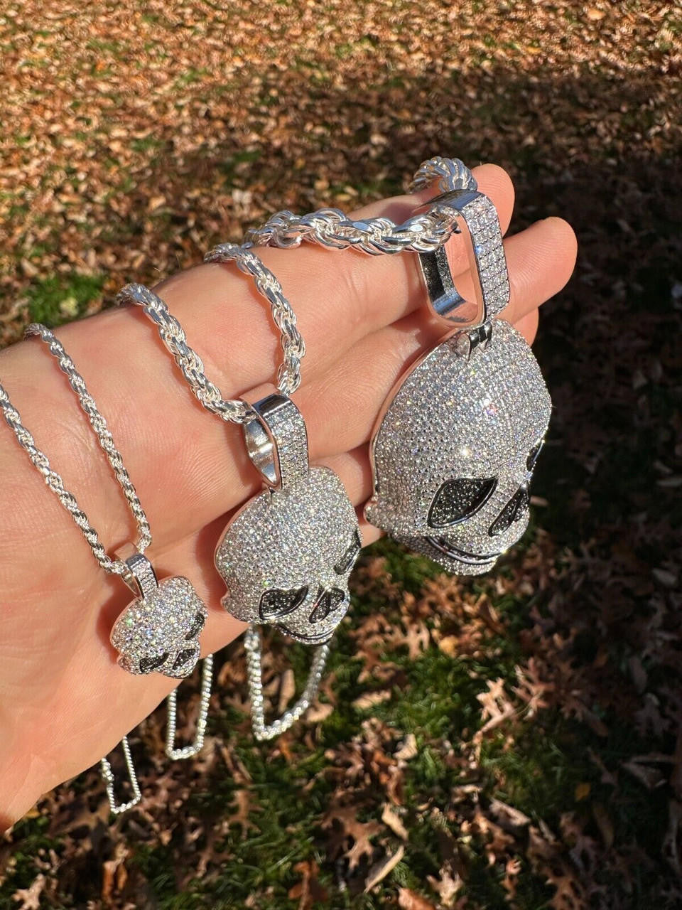 Hand holding three White Gold moissanite skull necklaces of different sizes with 14k White Gold Twisted Rope Chain