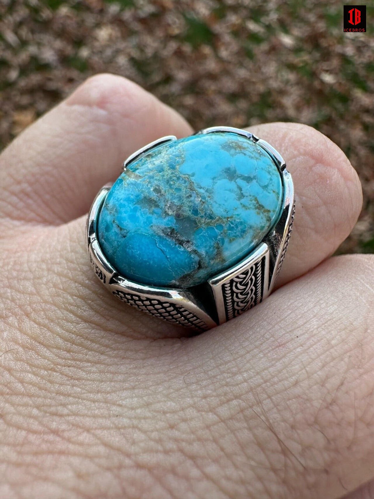 A man's hand showcasing a blue oval cut turquoise stone ring, exuding elegance and style.